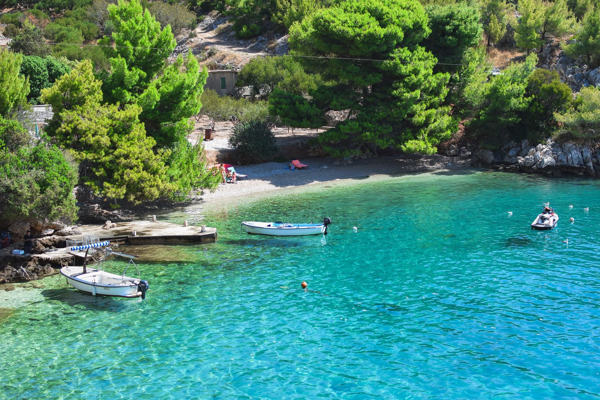Tirkizna uvala sa šljunčanom plažom, borovima na padini i malim brodicama